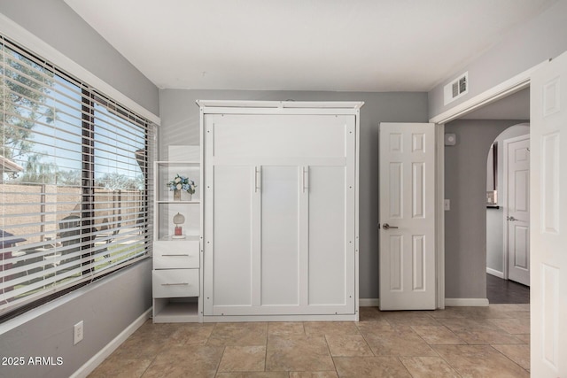 unfurnished bedroom with baseboards, visible vents, arched walkways, and a closet