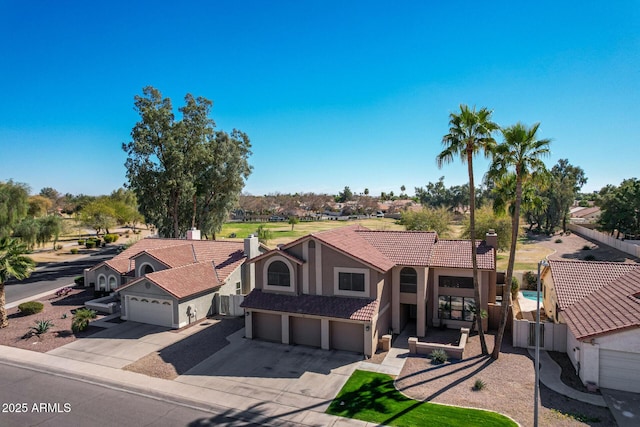 mediterranean / spanish home featuring an attached garage, a tile roof, driveway, stucco siding, and a chimney