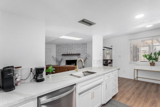 kitchen with light stone counters, open floor plan, white cabinetry, a sink, and dishwasher