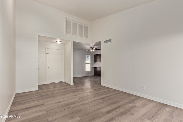 unfurnished room with a high ceiling, ceiling fan, and light wood-type flooring