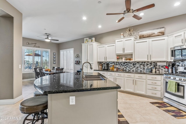 kitchen with sink, dark stone countertops, an island with sink, white cabinetry, and stainless steel appliances