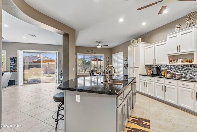 kitchen featuring dark stone countertops, a kitchen island with sink, sink, and white cabinets