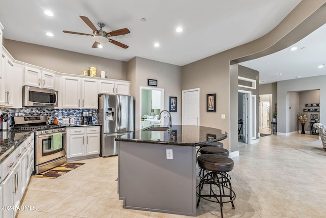 kitchen with sink, dark stone countertops, an island with sink, appliances with stainless steel finishes, and white cabinetry