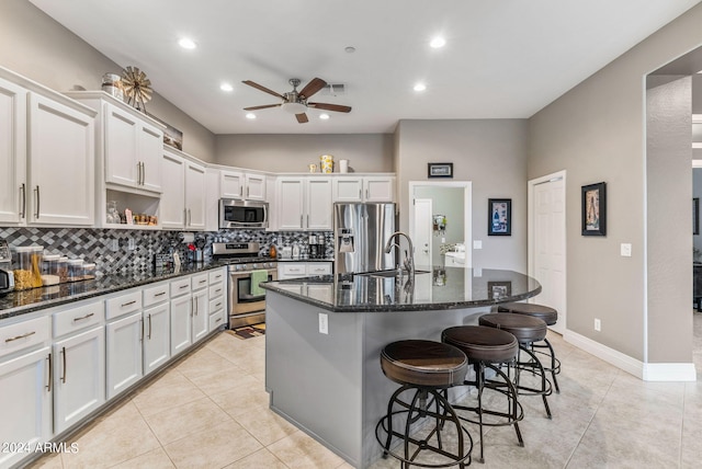 kitchen with stainless steel appliances, sink, a center island with sink, dark stone countertops, and white cabinets