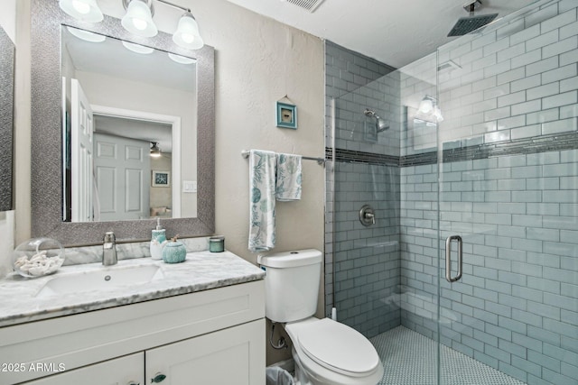 bathroom with toilet, vanity, a textured wall, and a shower stall