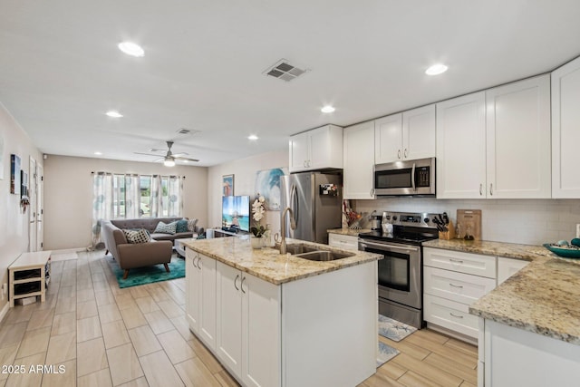 kitchen featuring a sink, appliances with stainless steel finishes, open floor plan, a kitchen island with sink, and decorative backsplash