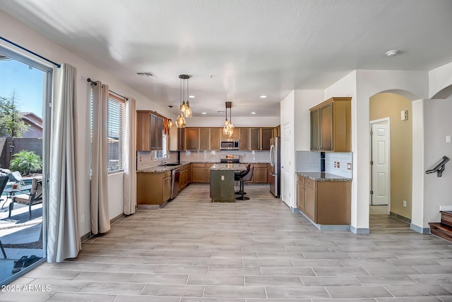11936 W Alvarado Rd, Avondale, AZ 85392 - kitchen featuring appliances with stainless steel finishes, arched walkways, tasteful backsplash, a kitchen island, and stone countertops