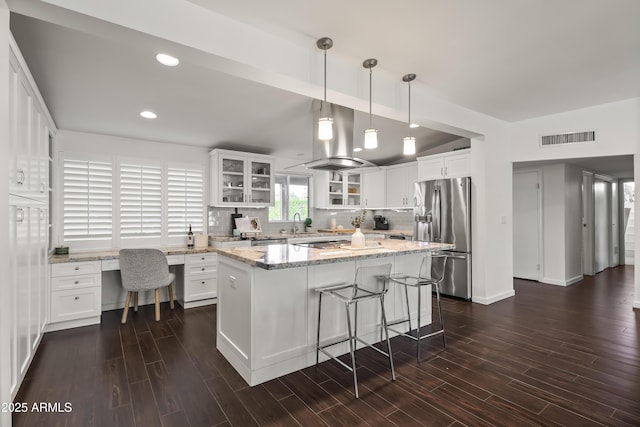 kitchen featuring light stone counters, a center island, stainless steel fridge, island exhaust hood, and white cabinets