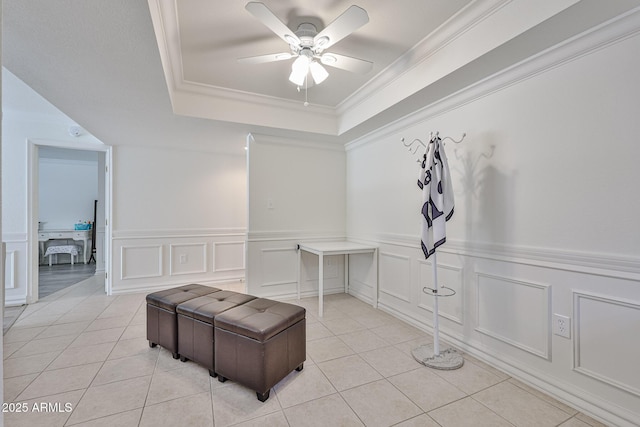 interior space with a tray ceiling, ornamental molding, a wainscoted wall, light tile patterned flooring, and ceiling fan