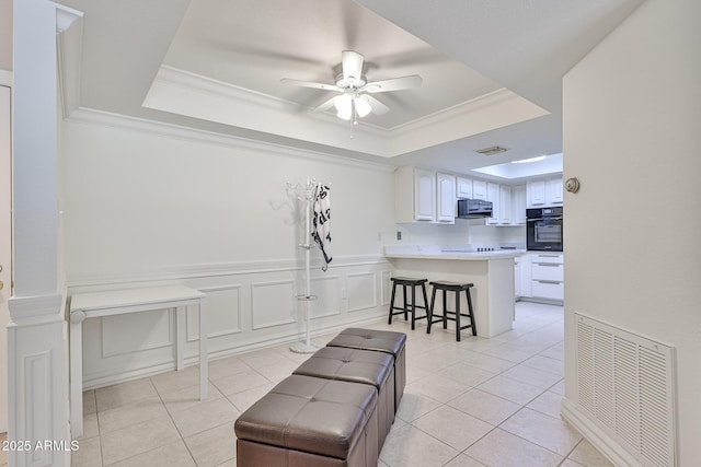 interior space with a raised ceiling, a kitchen breakfast bar, a peninsula, visible vents, and black appliances
