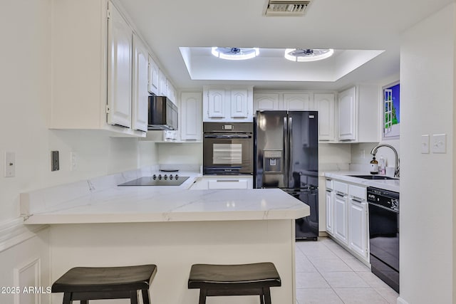 kitchen featuring black appliances, a raised ceiling, a sink, and a peninsula