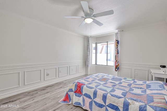 bedroom with light wood-type flooring, ornamental molding, a textured ceiling, a wainscoted wall, and ceiling fan