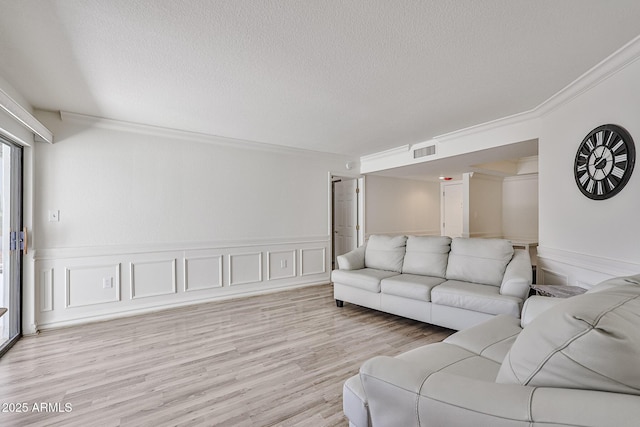 living area with a textured ceiling, visible vents, crown molding, light wood finished floors, and wainscoting