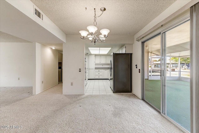 spare room with a textured ceiling, light carpet, and a notable chandelier