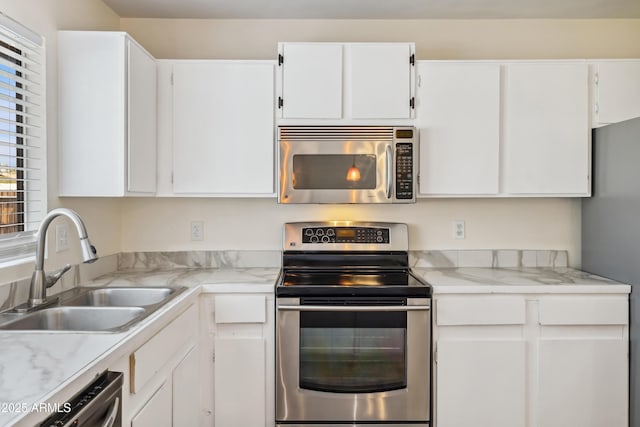 kitchen with appliances with stainless steel finishes, white cabinetry, light countertops, and a sink