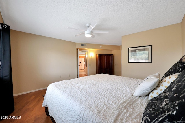 bedroom with a ceiling fan, baseboards, wood finished floors, visible vents, and a textured ceiling