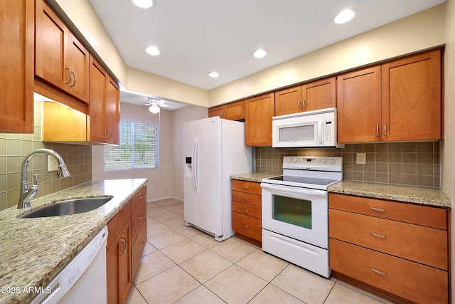 kitchen with brown cabinetry, light tile patterned floors, white appliances, and a sink