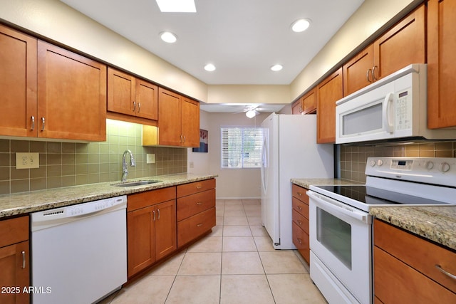 kitchen featuring white appliances, light tile patterned floors, a sink, brown cabinets, and backsplash