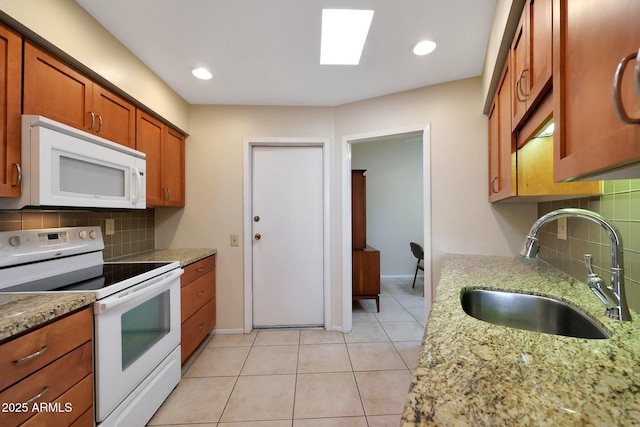 kitchen featuring backsplash, light tile patterned floors, brown cabinetry, white appliances, and a sink