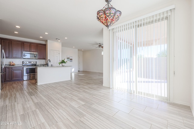 kitchen featuring ceiling fan with notable chandelier, stainless steel appliances, light stone countertops, pendant lighting, and a kitchen island with sink