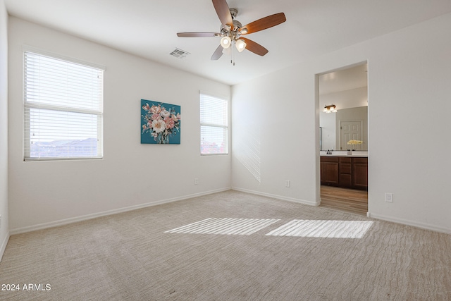 unfurnished bedroom featuring connected bathroom, light carpet, and ceiling fan