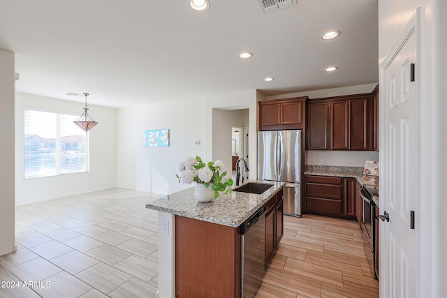 kitchen featuring stainless steel appliances, sink, light stone counters, a kitchen island with sink, and pendant lighting