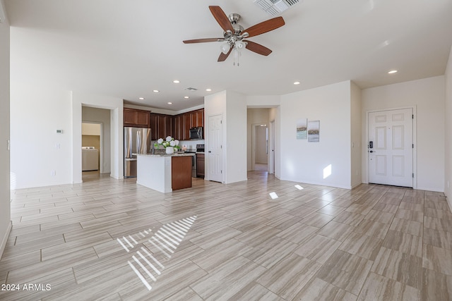 unfurnished living room featuring washer / dryer, ceiling fan, and light wood-type flooring