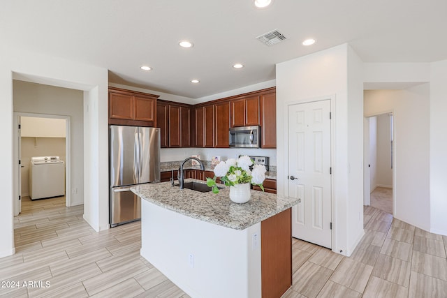 kitchen with light stone counters, washer / dryer, appliances with stainless steel finishes, sink, and a kitchen island with sink