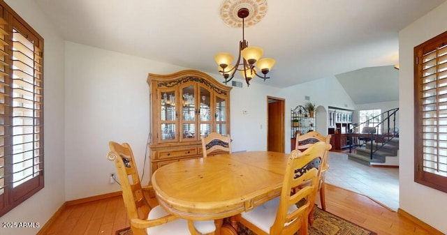 dining room featuring baseboards, stairway, vaulted ceiling, light wood-style floors, and a notable chandelier