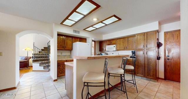 kitchen featuring white appliances, light tile patterned floors, visible vents, a kitchen island, and light countertops