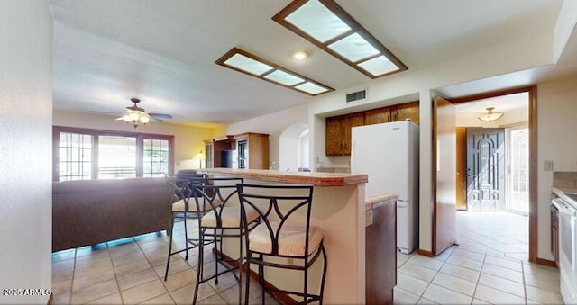 kitchen with visible vents, a breakfast bar, light countertops, light tile patterned floors, and brown cabinets