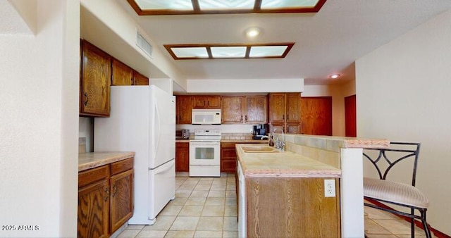 kitchen featuring a kitchen bar, a sink, white appliances, light tile patterned flooring, and light countertops