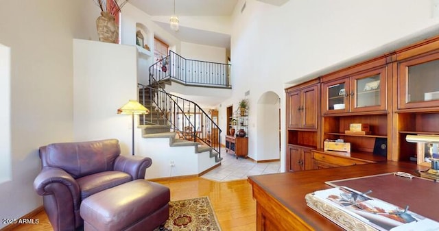 office space featuring arched walkways, light wood-type flooring, a high ceiling, and baseboards