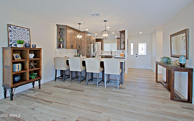 kitchen featuring tasteful backsplash, kitchen peninsula, light hardwood / wood-style floors, decorative light fixtures, and stainless steel refrigerator with ice dispenser