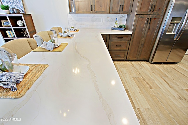 kitchen with light hardwood / wood-style floors, stainless steel refrigerator with ice dispenser, tasteful backsplash, and light stone counters