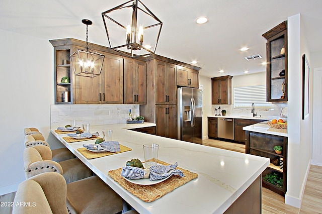 kitchen with decorative backsplash, hanging light fixtures, kitchen peninsula, light wood-type flooring, and appliances with stainless steel finishes