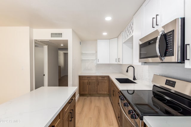 kitchen with light stone countertops, white cabinetry, sink, stainless steel appliances, and light hardwood / wood-style floors