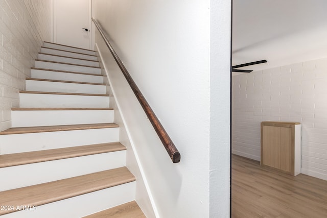 staircase with hardwood / wood-style flooring and brick wall