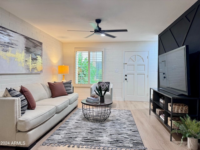 living room featuring light hardwood / wood-style floors, ceiling fan, and brick wall