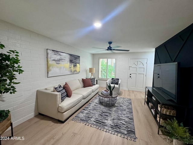 living room with ceiling fan, light hardwood / wood-style floors, and brick wall