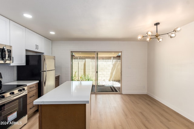 kitchen with light wood-type flooring, stainless steel appliances, a notable chandelier, white cabinets, and hanging light fixtures