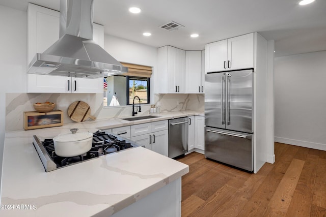 kitchen with sink, wall chimney exhaust hood, stainless steel appliances, white cabinets, and light wood-type flooring