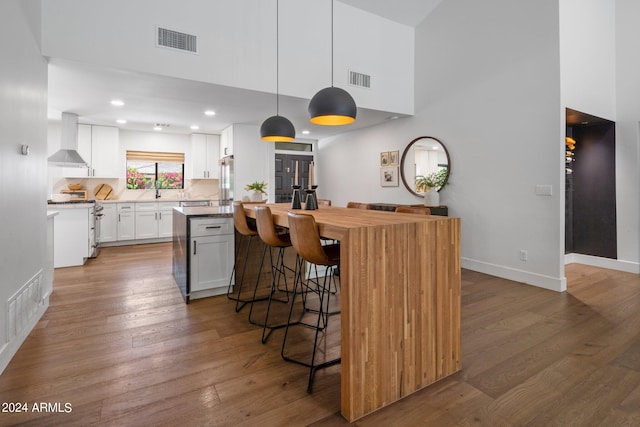 kitchen featuring dark hardwood / wood-style flooring, wall chimney range hood, white cabinets, a center island, and hanging light fixtures