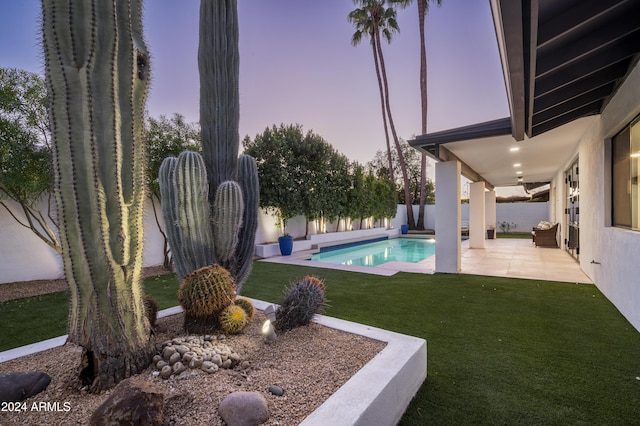 pool at dusk featuring a lawn and a patio area