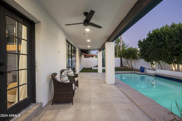 pool at dusk with ceiling fan and a patio