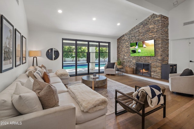 living room featuring beamed ceiling, high vaulted ceiling, a stone fireplace, and hardwood / wood-style flooring