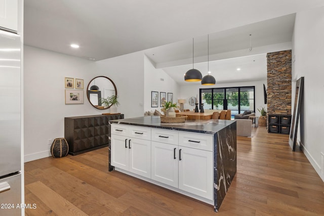 kitchen with high end refrigerator, white cabinets, vaulted ceiling, decorative light fixtures, and light hardwood / wood-style floors