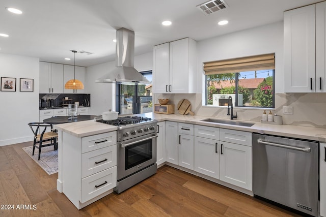 kitchen with sink, hanging light fixtures, island exhaust hood, white cabinets, and appliances with stainless steel finishes