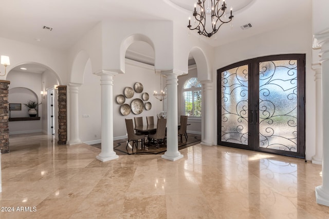 entrance foyer with a chandelier, ornate columns, and french doors