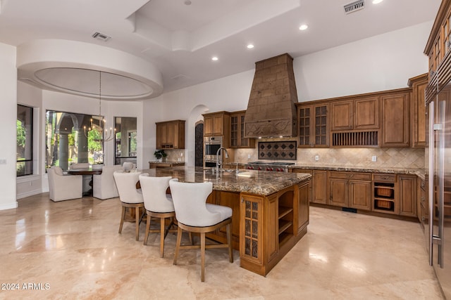 kitchen featuring a center island with sink, an inviting chandelier, sink, custom exhaust hood, and a breakfast bar